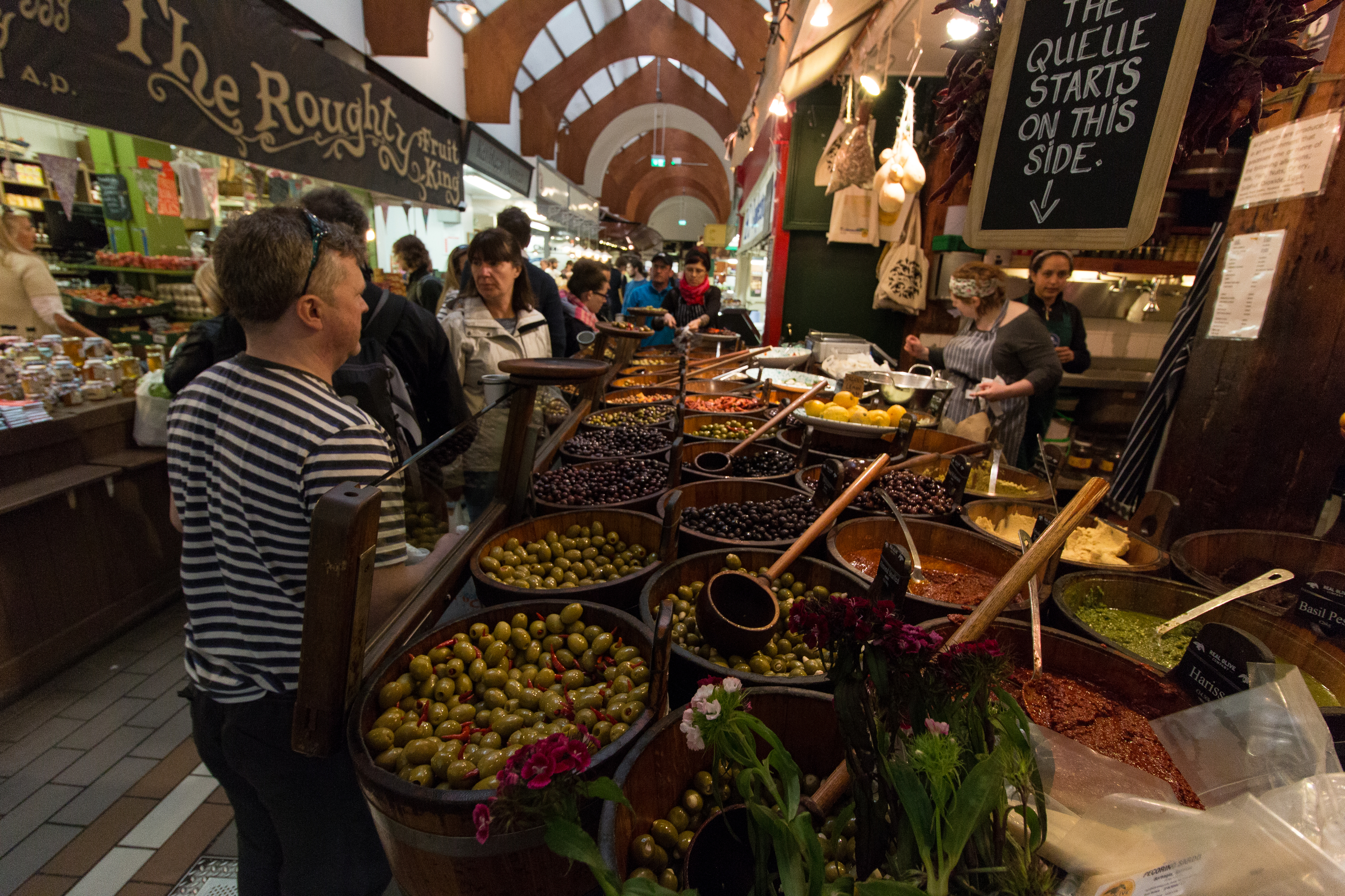 Busy aisle inside Cork's English Market with food counters, shoppers and Roughty Foodie in the background.